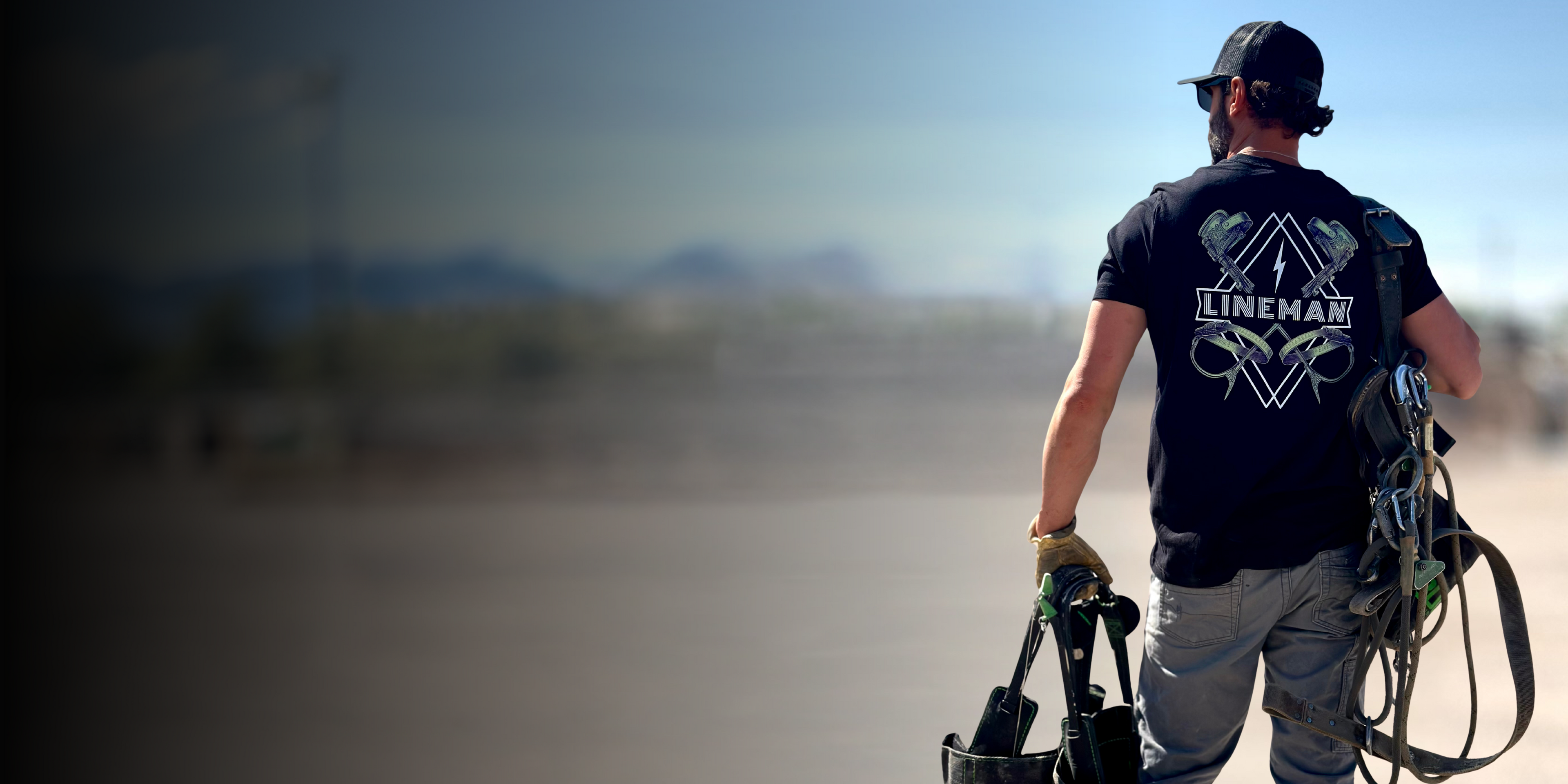 Lineman carrying climbing gear wearing a "lineman" shirt.