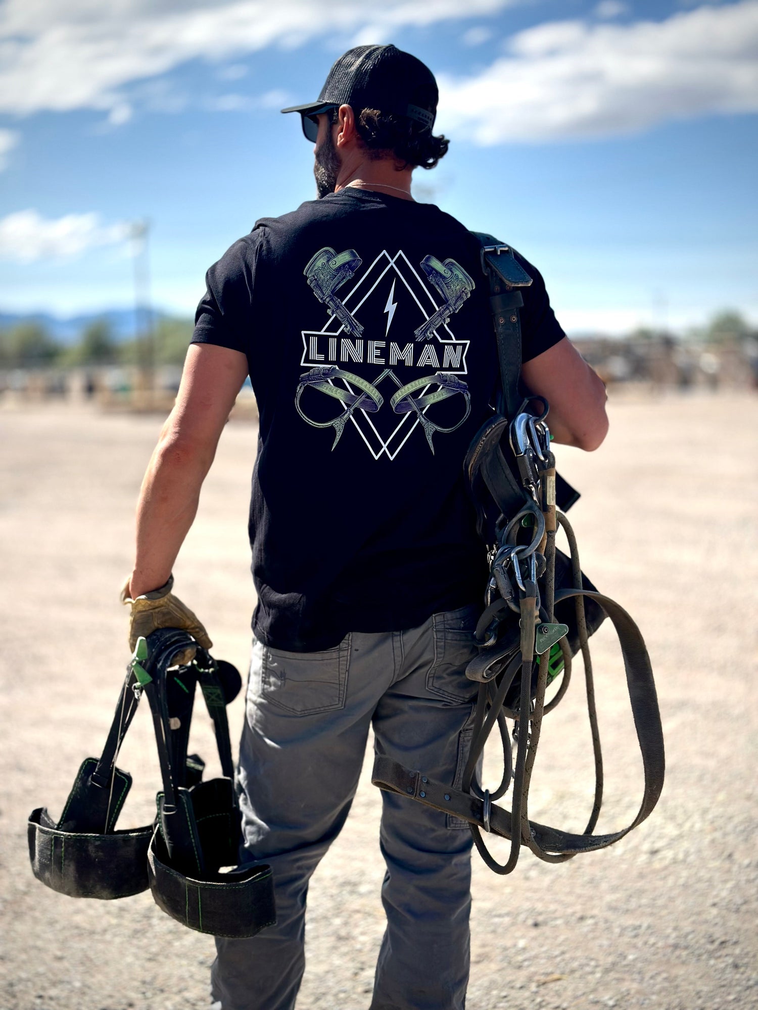 Lineman wearing black lineman shirt with linemen climbing gear on it.